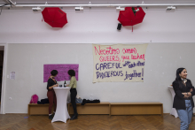 Zwei Menschen im Raum. Hinter ein Banner "Nosotros somos queer que luchan.."